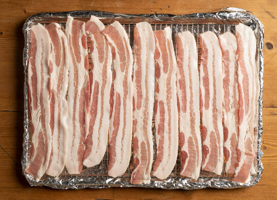 uncooked baccon on a foil lined cooking rack