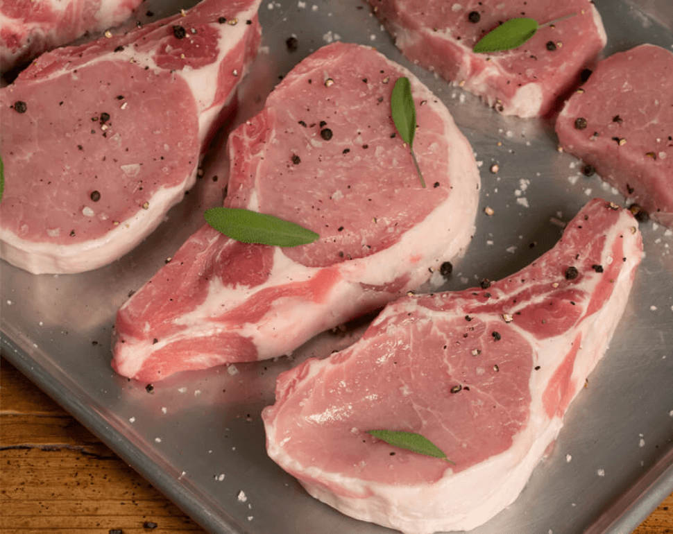 raw pork chops with seasoning on a metal pan