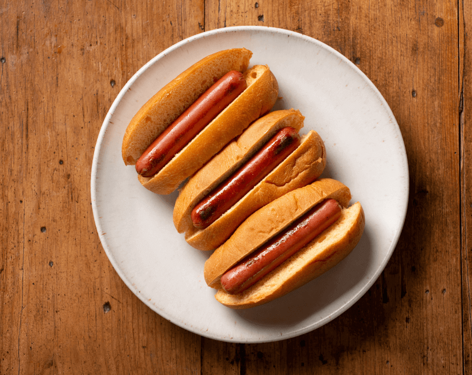 Three hot dogs in buns sitting on a white plate