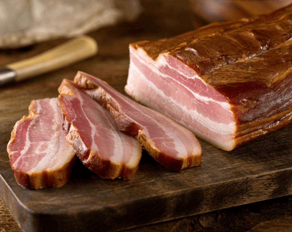 A large piece of pork being sliced into bacon