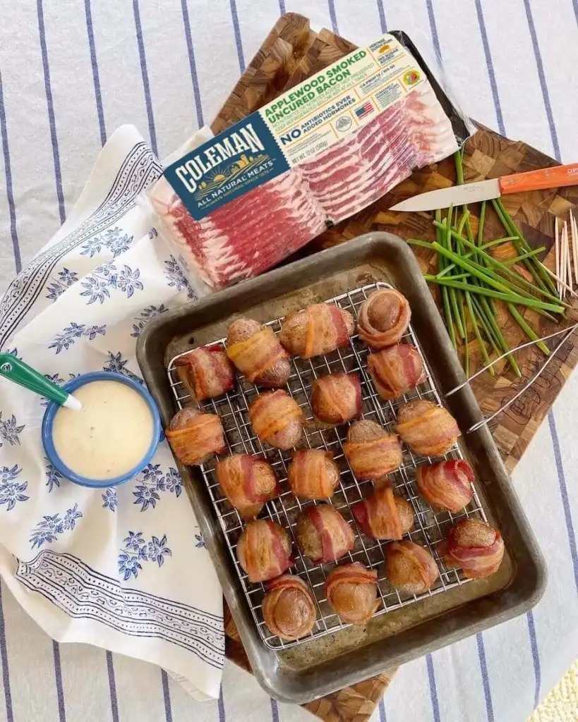Bacon wrapped sausages on a baking trey next to a package of bacon
