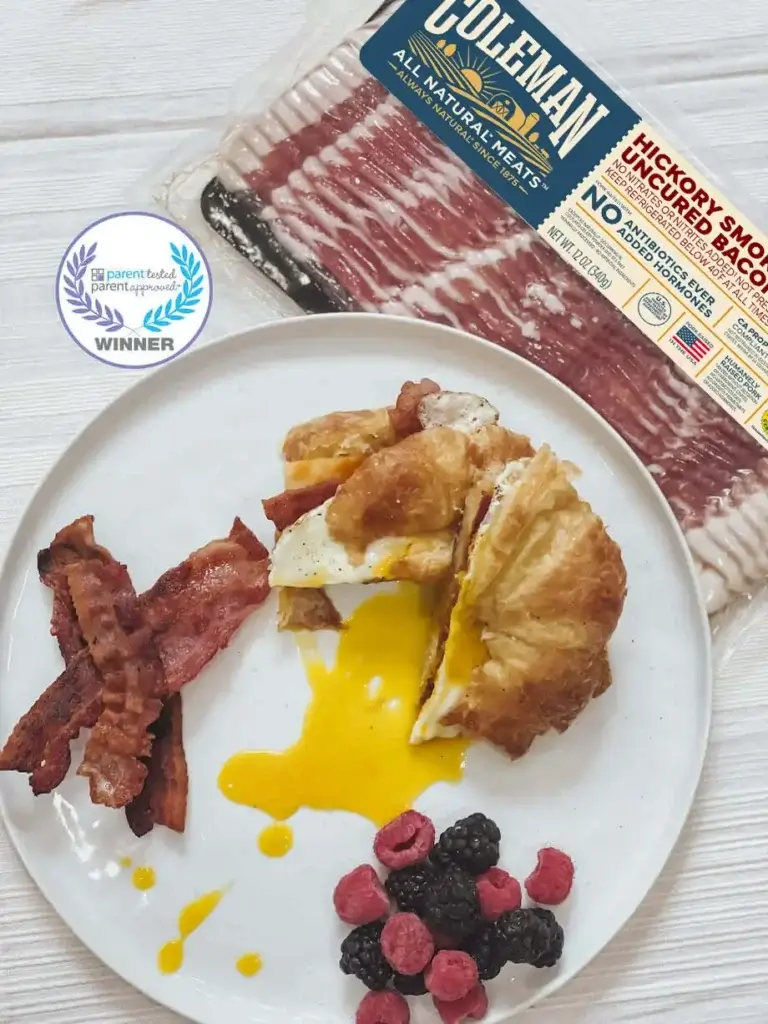 Hickory smoked bacon next to a plate with a breakfast croissant and berries