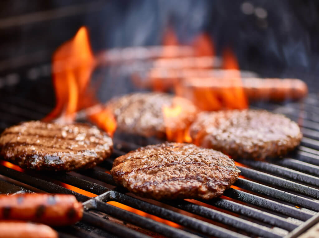 Hamburgers and hot dogs cooking on grill with flames